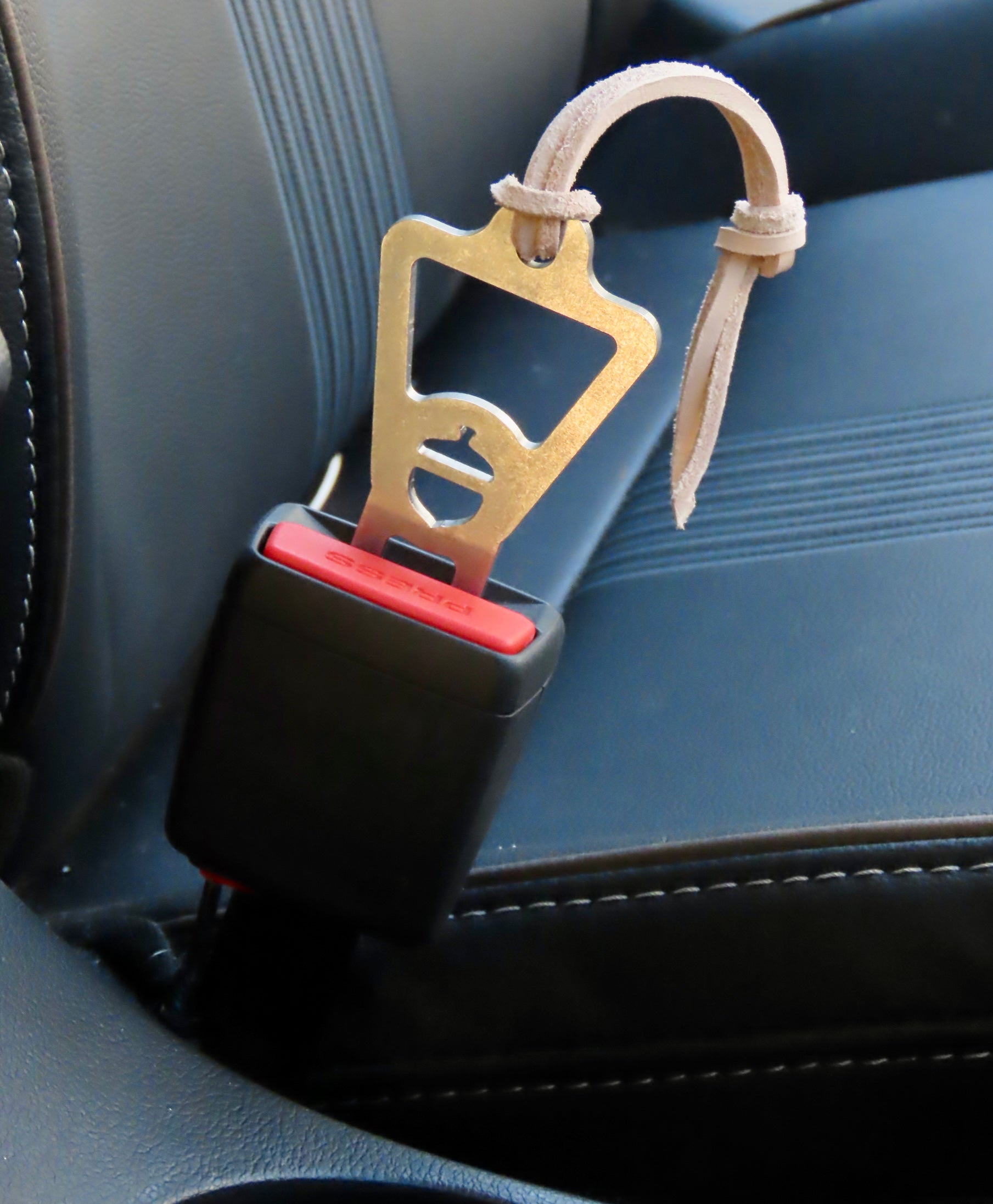 Car seat belt clip with bottle opener attached to a car seat.