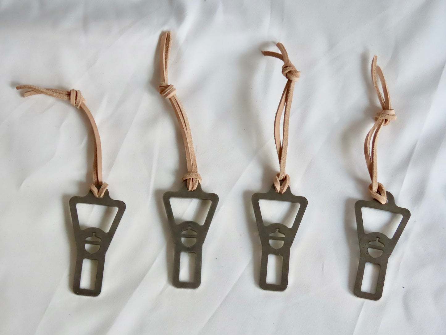 Four metal bottle openers with leather straps on a white background